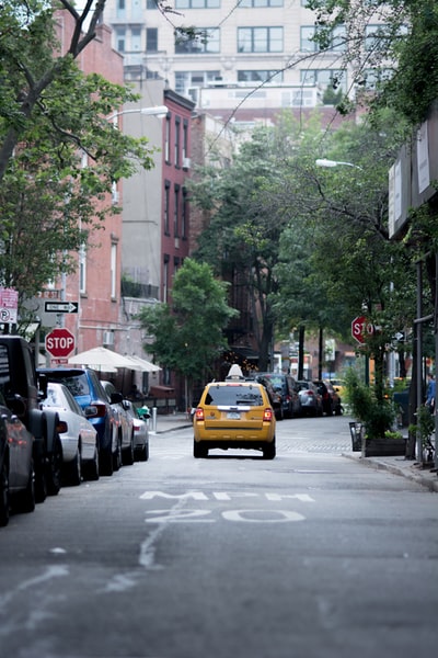 白天，黄色出租车开在靠近建筑物和树木的灰色水泥路面上